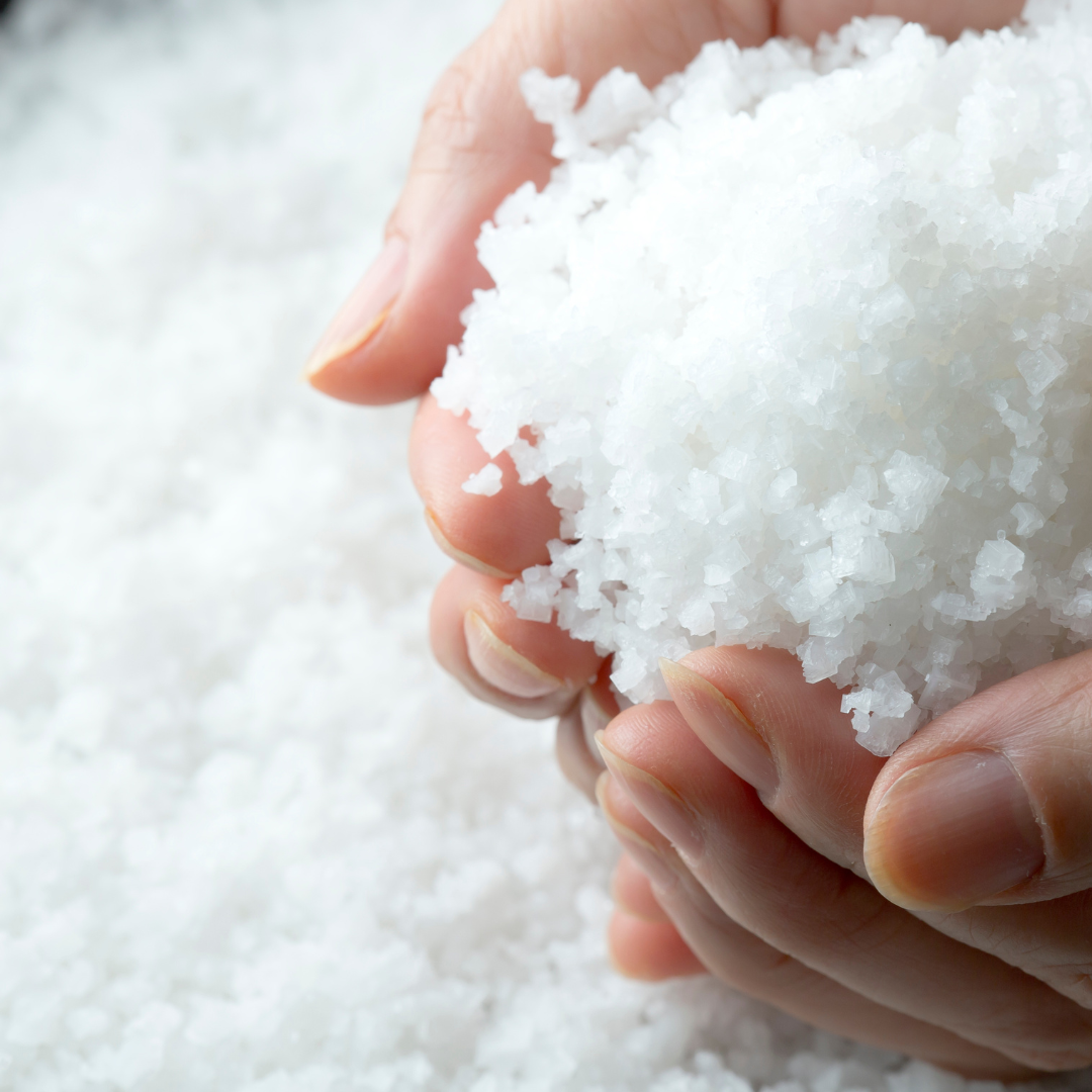 A person holding a handful of coarse sea salt.